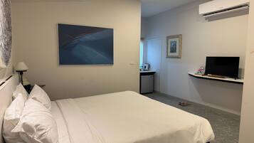 A hotel room with a bed, a television, an air conditioner, and a painting on the wall.