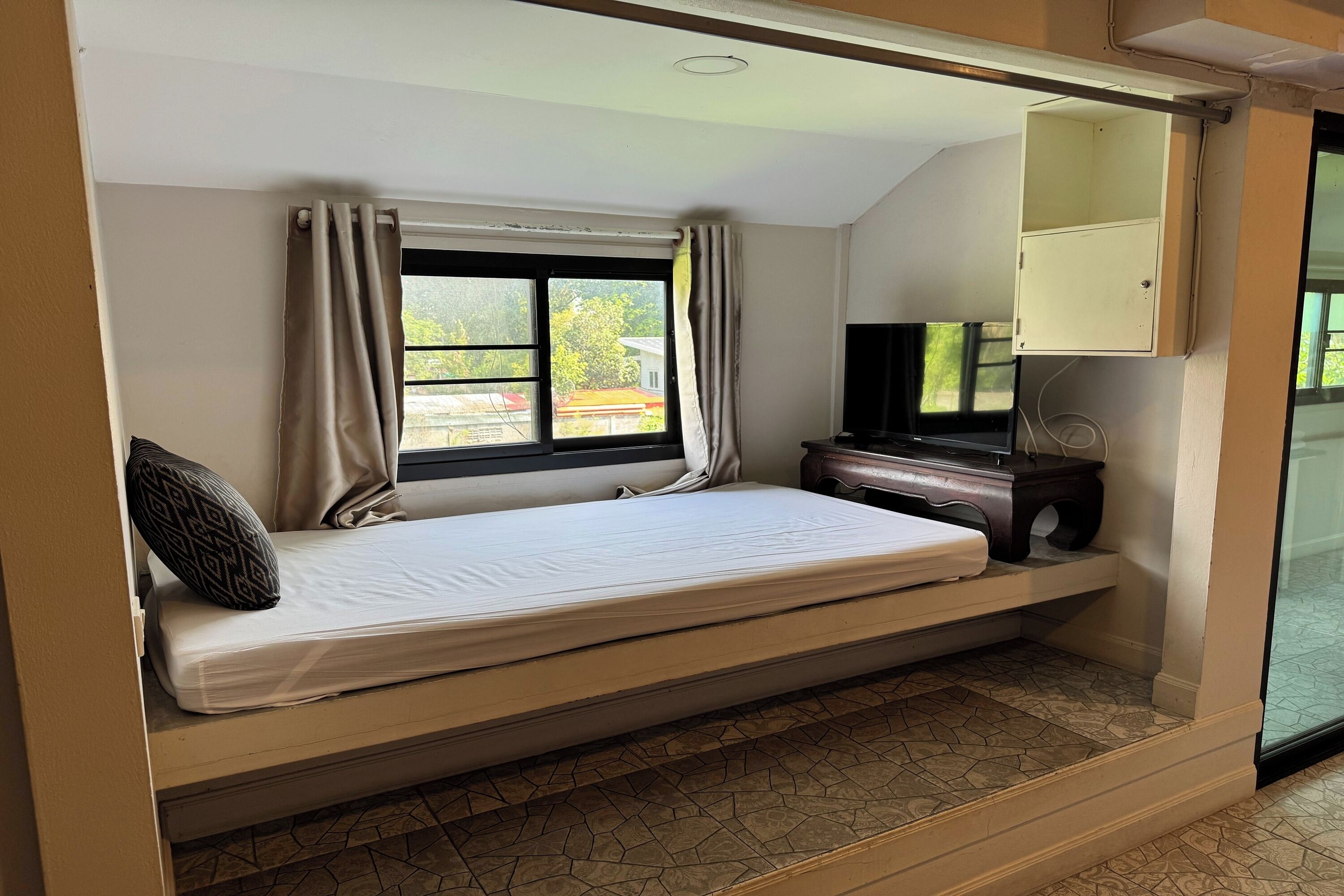 A room with a bed, a television, a cabinet, and a window with curtains.