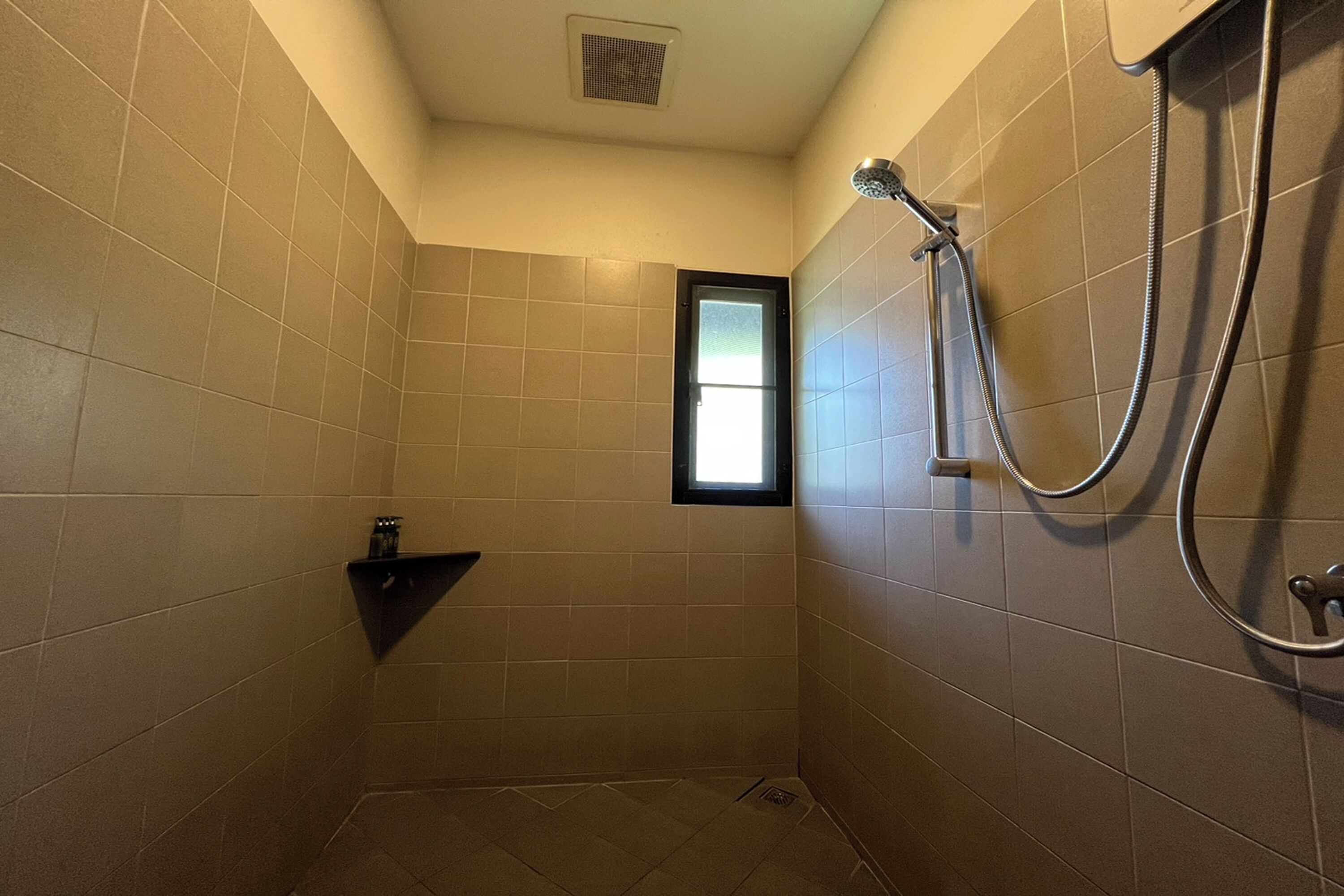 A small, tiled bathroom with a shower, a window, and a towel rack.