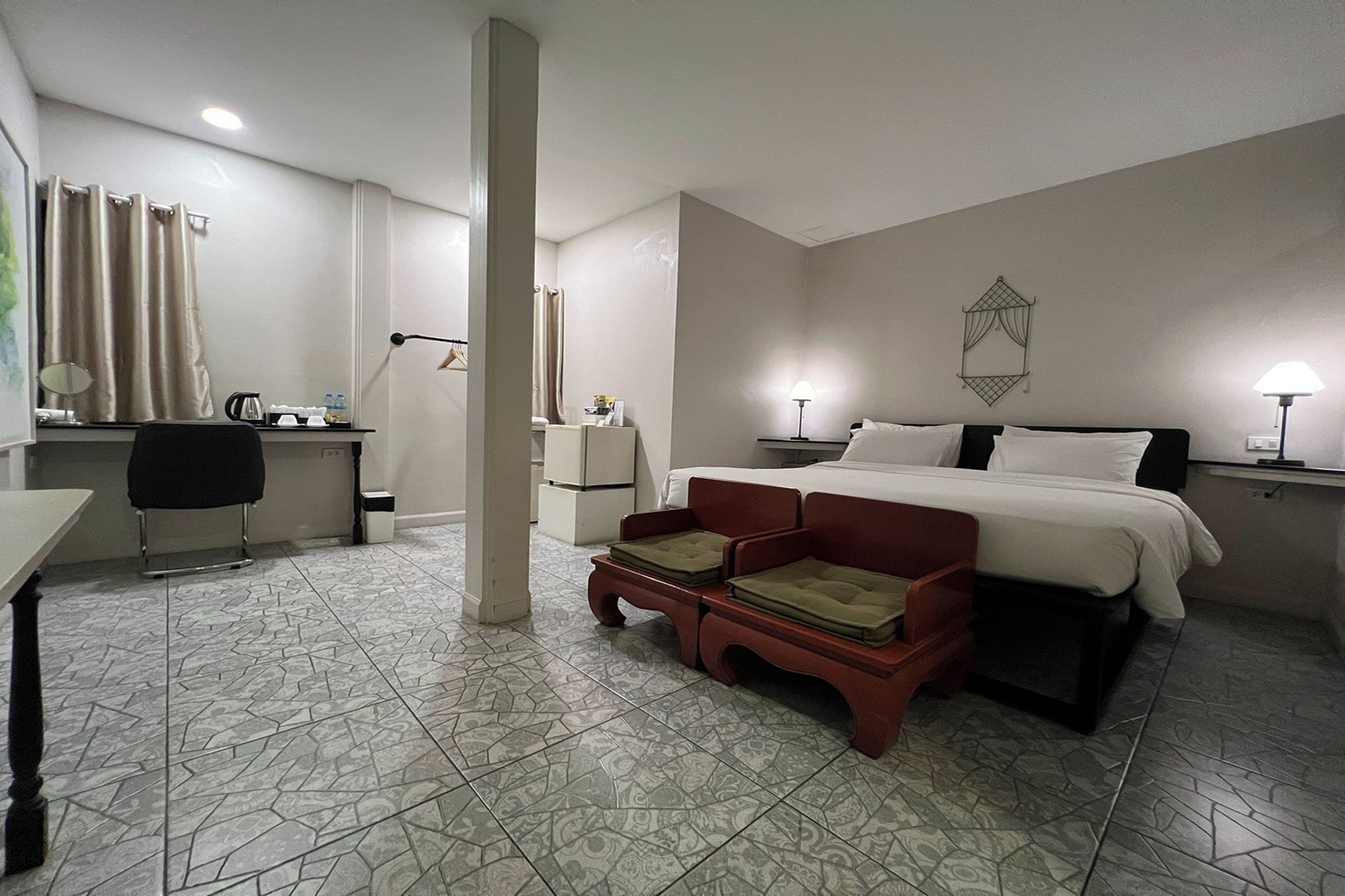 Quarto de hotel com cama, escrivaninha, cadeira e uma pequena mesa com abajur.