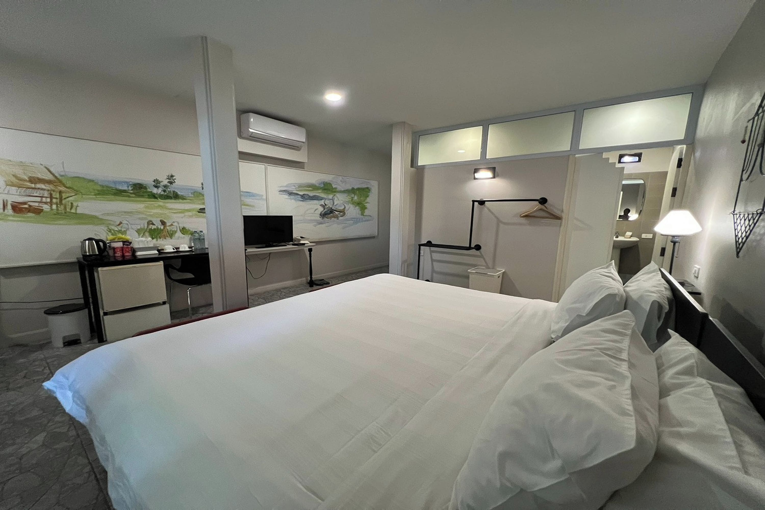 A hotel room with a bed, a desk, a television, and a painting on the wall.