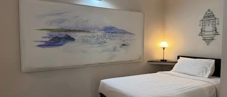 Un dormitorio con una cama, una mesita de noche, una lámpara de pared y un cuadro de paisaje grande.