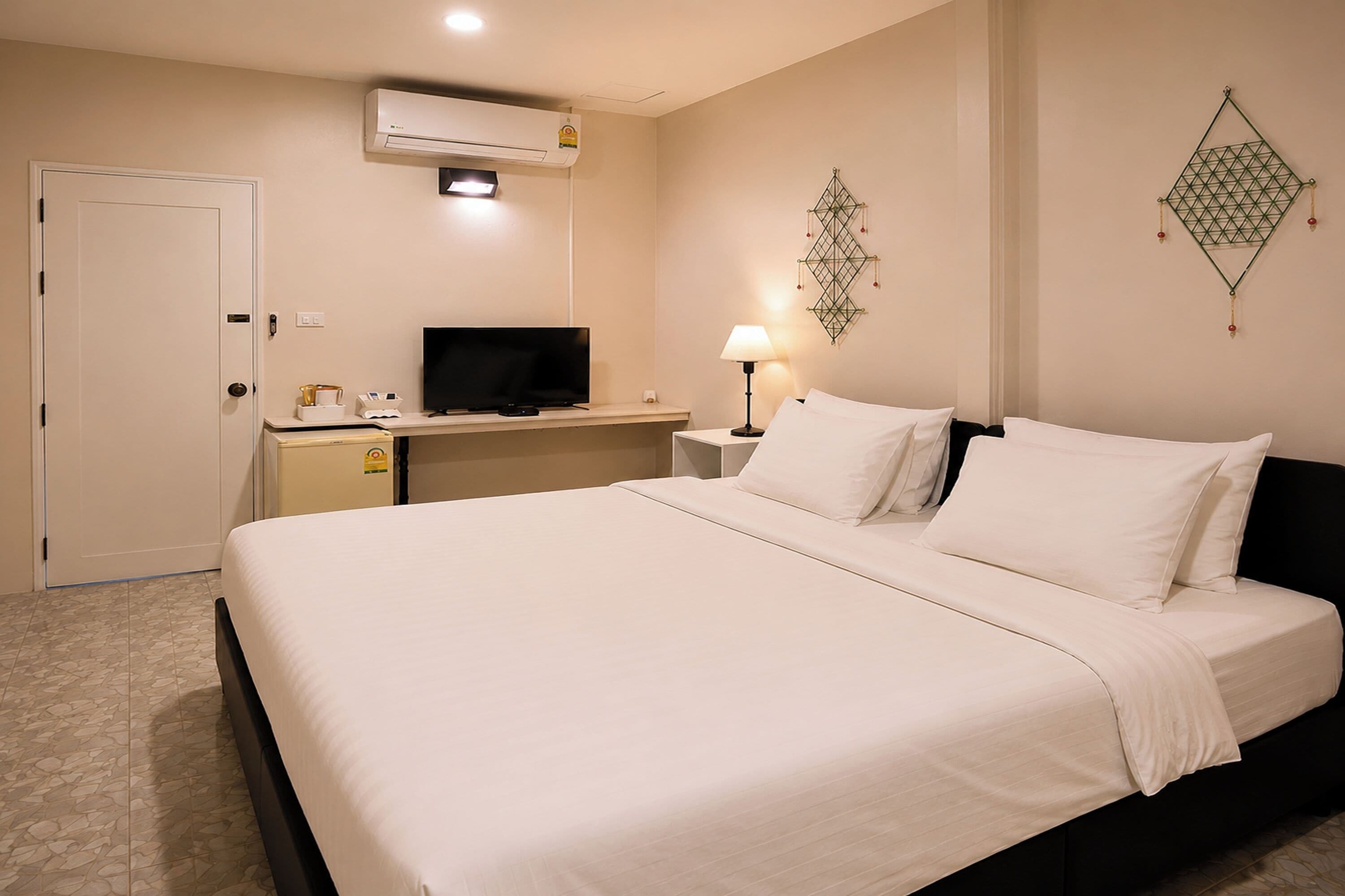 Una habitación de hotel con una cama, un escritorio con televisor, una lámpara y un equipo de aire acondicionado.