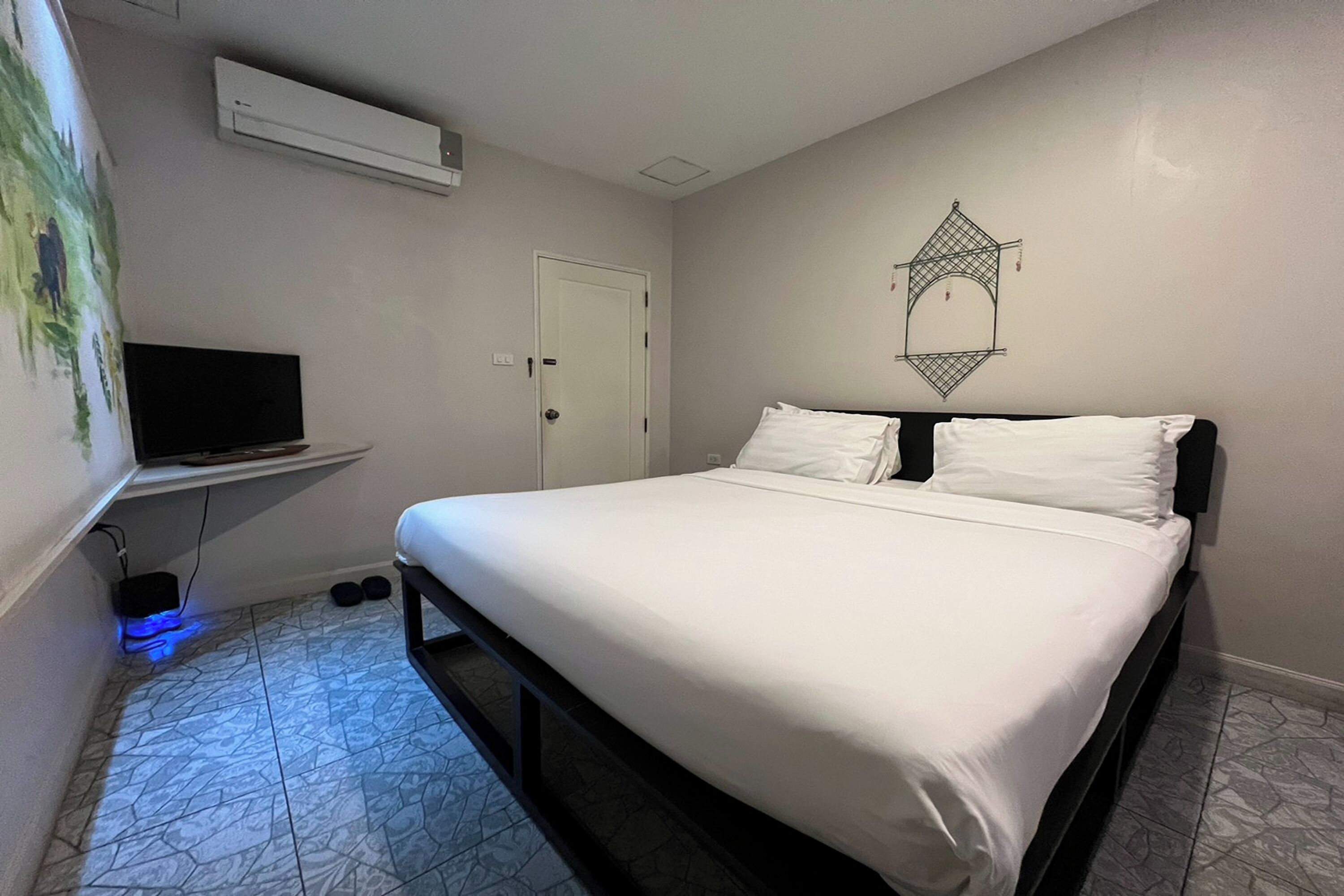 Um quarto com uma cama, uma TV em um suporte, uma porta e um enfeite na parede.