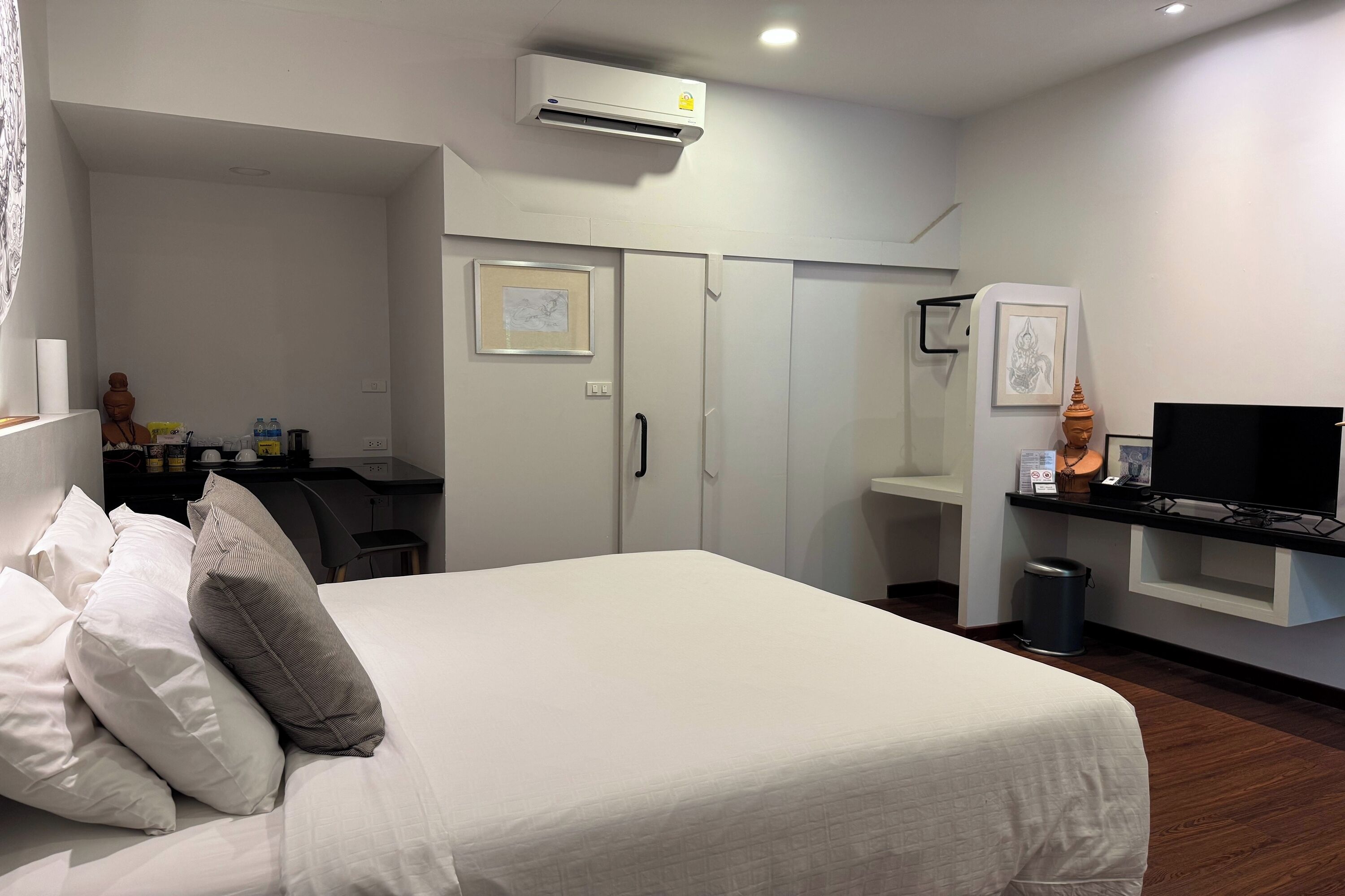 A hotel room with a bed, a desk, a TV, and a trash can.