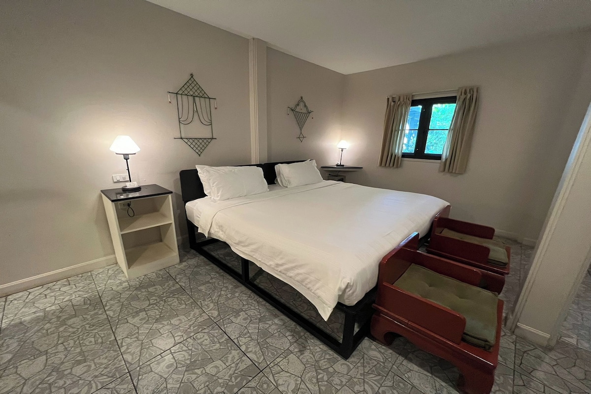A bedroom with a bed, bedside tables, a window with curtains, and patterned floor tiles.
