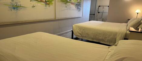 A hotel room with two beds, a painting on the wall, a lamp, and a small table.