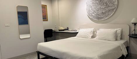 Una habitación de hotel moderna con una cama, un escritorio, una silla, un adorno redondo en la pared y un espejo.
