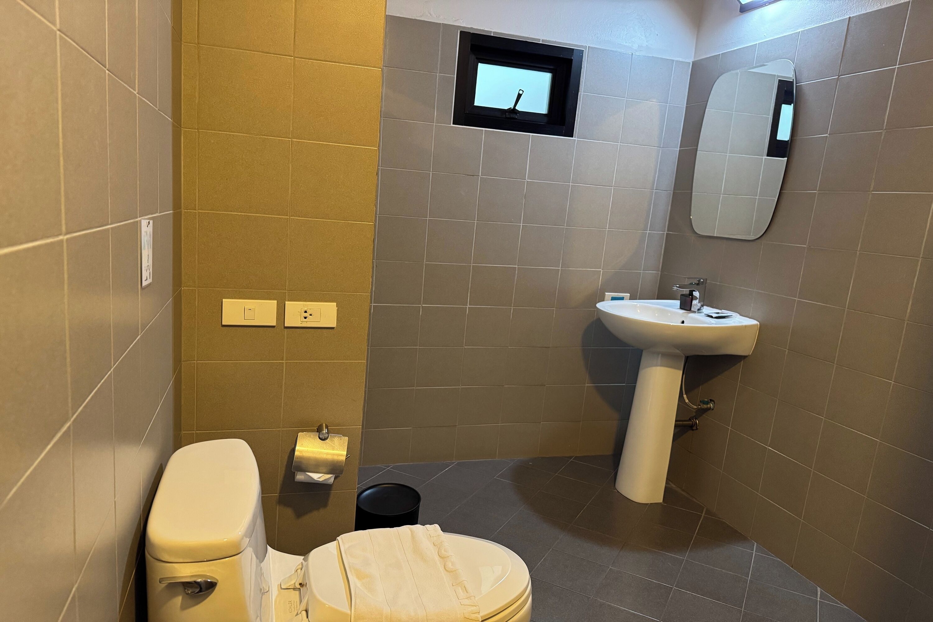 Een badkamer met toilet, wastafel, spiegel en een klein raam.