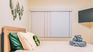 Une chambre d’hôtel avec un lit, des oreillers, un téléviseur fixé au mur et une fenêtre avec des stores.