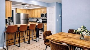 Une cuisine moderne avec des meubles en bois, des appareils électroménagers en acier inoxydable et un coin bar avec des tabourets.