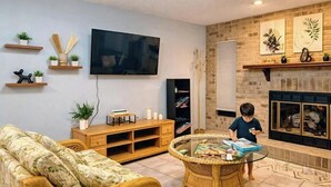 Un salon comprenant une télévision, des étagères avec des plantes, une cheminée, un canapé et une table basse.