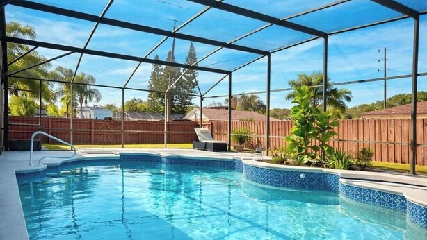 Une piscine avec un bord carrelé, une clôture en bois et un ciel dégagé.