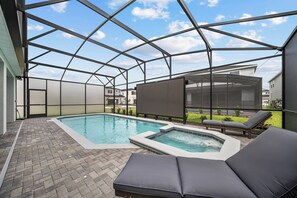 A covered outdoor swimming pool with lounge chairs, a hot tub, and a view of neighboring houses.