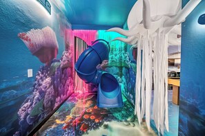 Una habitación de temática submarina con un mural, un tentáculo en el techo y un cubo azul.