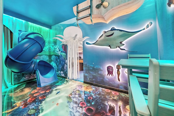 A children's play area with a slide, a mural of sea creatures, and a wooden ladder.