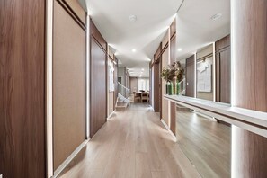 A hallway with wooden paneling, a light wooden floor, and a staircase leading to another room.