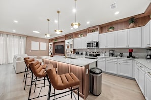 Una cocina moderna con una isla central, taburetes de bar, armarios blancos y electrodomésticos integrados.