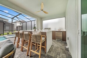Et udendørs køkkenområde med ventilator, pool og et siddeområde med stole og bord.