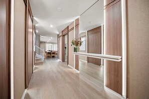 Un corridoio con pannelli di legno, una scala, una sala da pranzo e uno specchio che riflette l'ambiente.