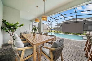 A wooden table with chairs, a pool, and a greenhouse structure.