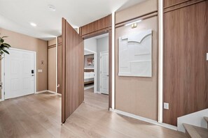 A hallway with wooden paneling, a white door, and a bed in the background.