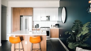 A modern kitchen with wooden cabinets, stainless steel appliances, and a central island with two orange bar stools. - Top-Floor 1BR Loft | Skyline Views | Walkable LoHi Denver (Denver)