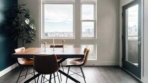 A dining area with a table, chairs, a plant, and large windows with a city view. - Top-Floor 1BR Loft | Skyline Views | Walkable LoHi Denver (Denver)