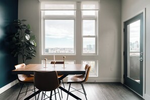 A dining area with a table, chairs, a plant, and large windows with a city view. - Top-Floor 1BR Loft | Skyline Views | Walkable LoHi Denver (Denver)