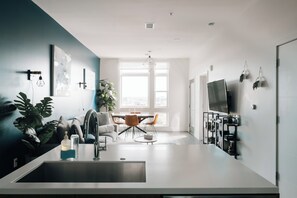 A modern kitchen with a sink, dining table, chairs, and a TV. - Top-Floor 1BR Loft | Skyline Views | Walkable LoHi Denver (Denver)
