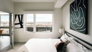 A modern bedroom with a large window, a bed, and abstract wall art. - Top-Floor 1BR Loft | Skyline Views | Walkable LoHi Denver (Denver)