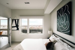 A modern bedroom with a large window, a bed, and abstract wall art. - Top-Floor 1BR Loft | Skyline Views | Walkable LoHi Denver (Denver)