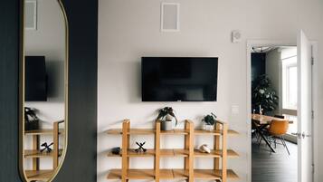 Una sala de estar moderna con un espejo grande, estanterías de madera, un televisor de pantalla plana y un comedor con mesa y sillas.