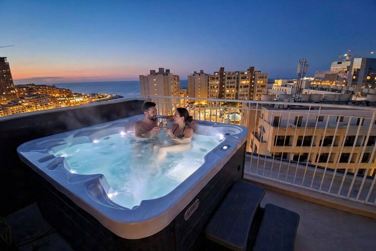 Un jacuzzi con vista a la ciudad, un balcón con barandilla y una zona de estar.