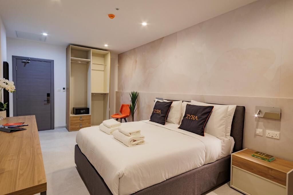 A modern hotel room with a bed, bedside tables, a desk, and a wardrobe.