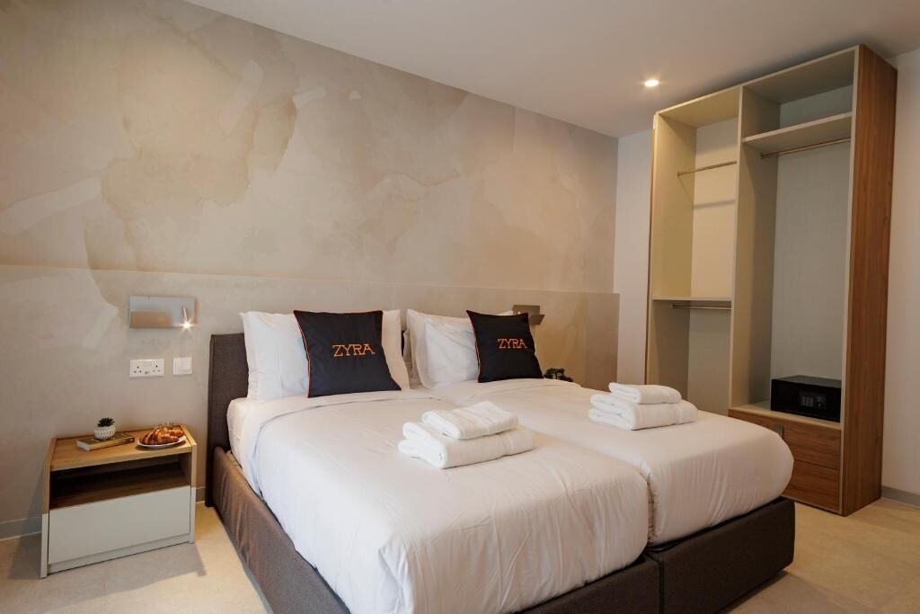 A hotel room with two beds, a wardrobe, a bedside table, and a wall-mounted light.