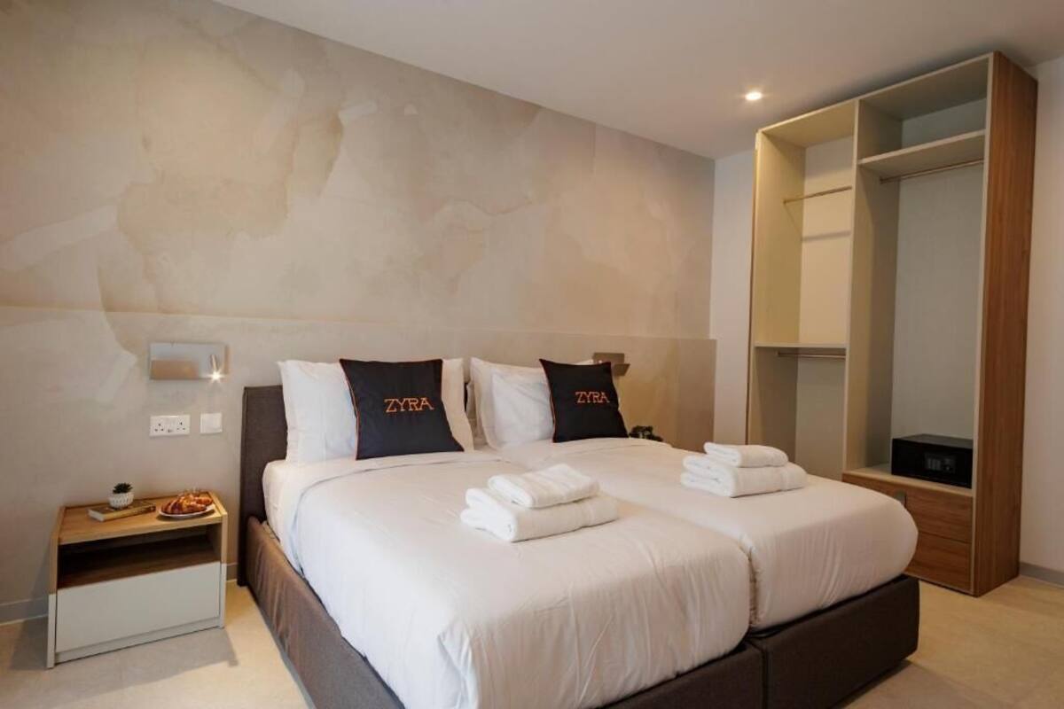 Habitación de hotel con dos camas, un armario, una mesita de noche y una lámpara de pared.