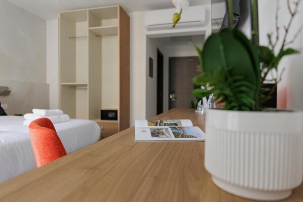 A hotel room with a wooden table, two beds, a white vase with a plant, and a magazine. - Zyra Hotel St. Julians (St. Julian's)