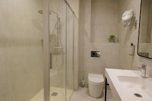 Um banheiro moderno com chuveiro em box de vidro, pia branca, vaso sanitário e um pequeno vaso com planta.