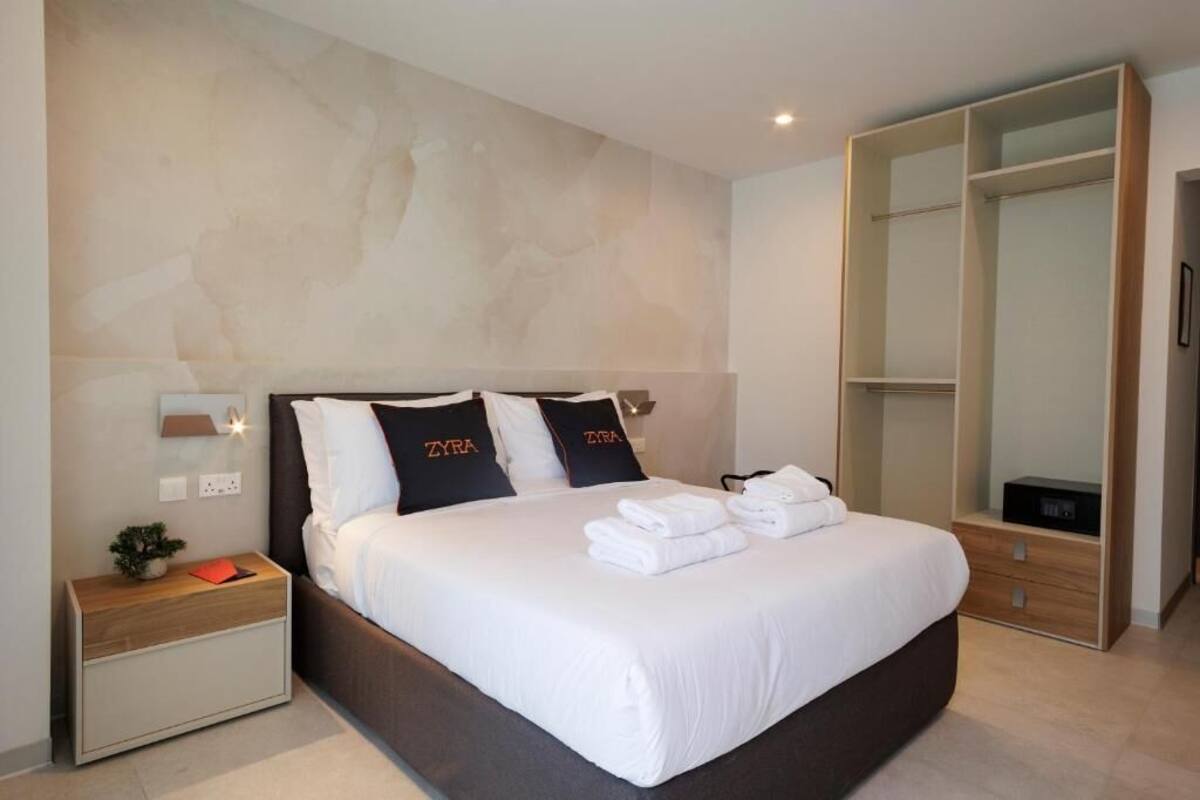 Una habitación de hotel moderna con una cama grande, una mesita de noche, un armario y una lámpara de pared.