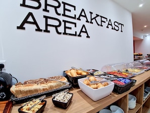 Un área de desayuno con un letrero que dice 'BREAKFAST AREA', diferentes alimentos y una máquina de café.