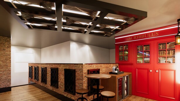 Un espace bar avec des tabourets, un comptoir et une bibliothèque rouge sur laquelle est inscrit le mot « SCRIBBULUS ».