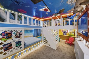 Ein Kinderzimmer mit Stockbetten, einer Rutsche und thematisch passenden Wanddekorationen.