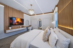 A modern bedroom with a large bed, a TV displaying a fire, a chandelier, and wooden paneling. - 8BR house sleeps 24 near Disney area (Clermont)