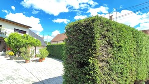 Ett bostadsområde med en stenlagd innergård, krukväxter, en välskött häck och ett hus med en balkong.