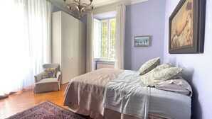 Ein Schlafzimmer mit einem Bett, einem Sessel, einem Fenster und einer Chandelüster.