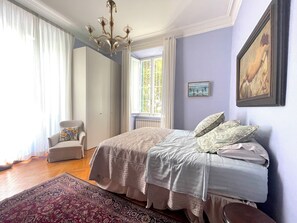 Ein Schlafzimmer mit einem Bett, einem Sessel, einem Fenster und einer Chandelüster.