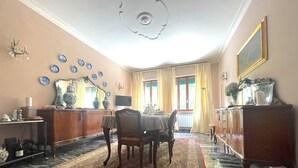 Ein Essbereich mit Tisch, Stühlen, einem gemusterten Teppich, einem Spiegel und einer Deckenleuchte.