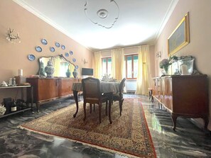 Ein Essbereich mit Tisch, Stühlen, einem gemusterten Teppich, einem Spiegel und einer Deckenleuchte.