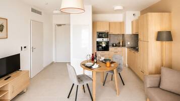 A modern kitchen with wooden cabinets, a dining table with chairs, a TV, and a sofa.